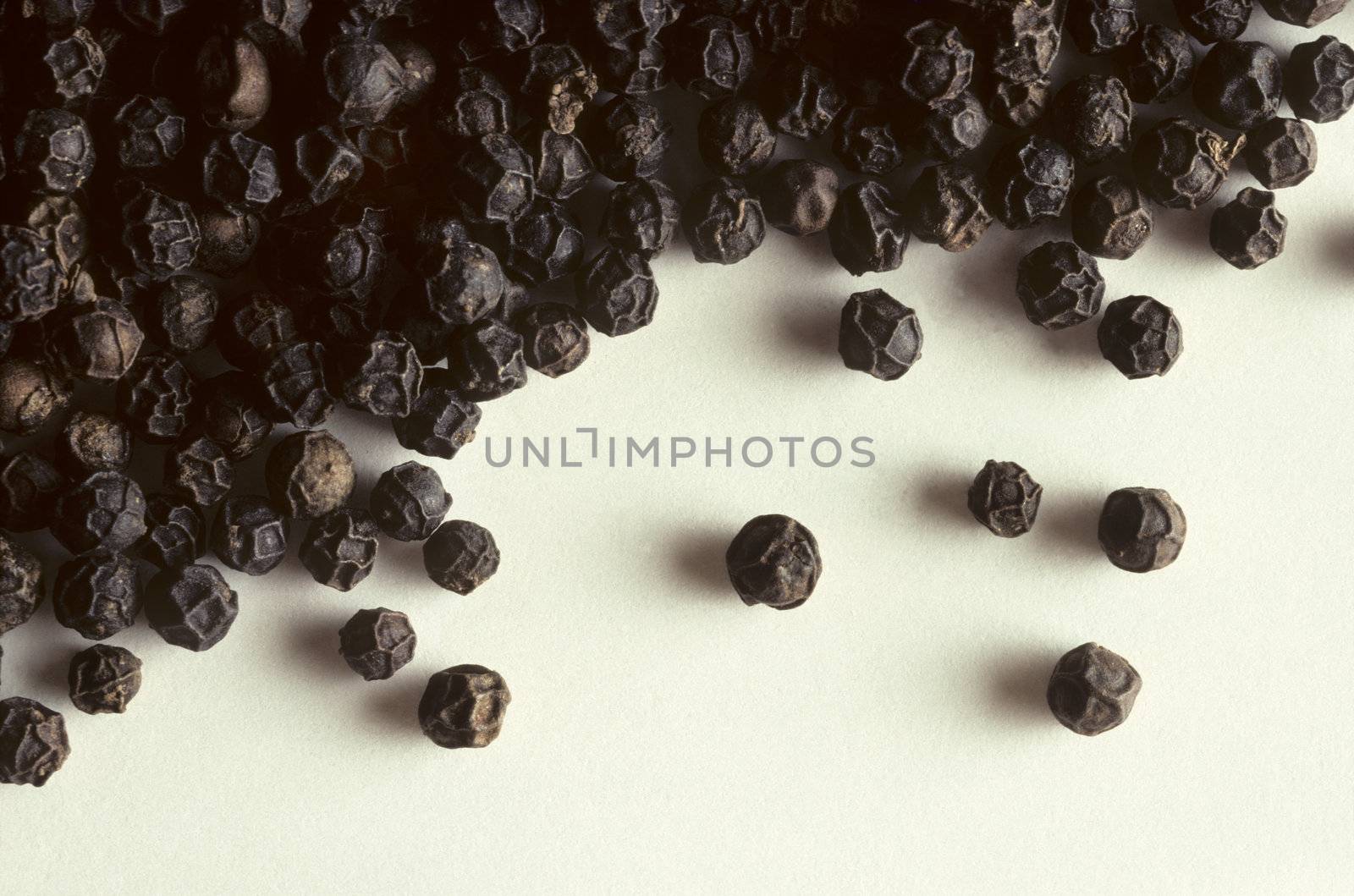 Whole black peppercorns on a white surface