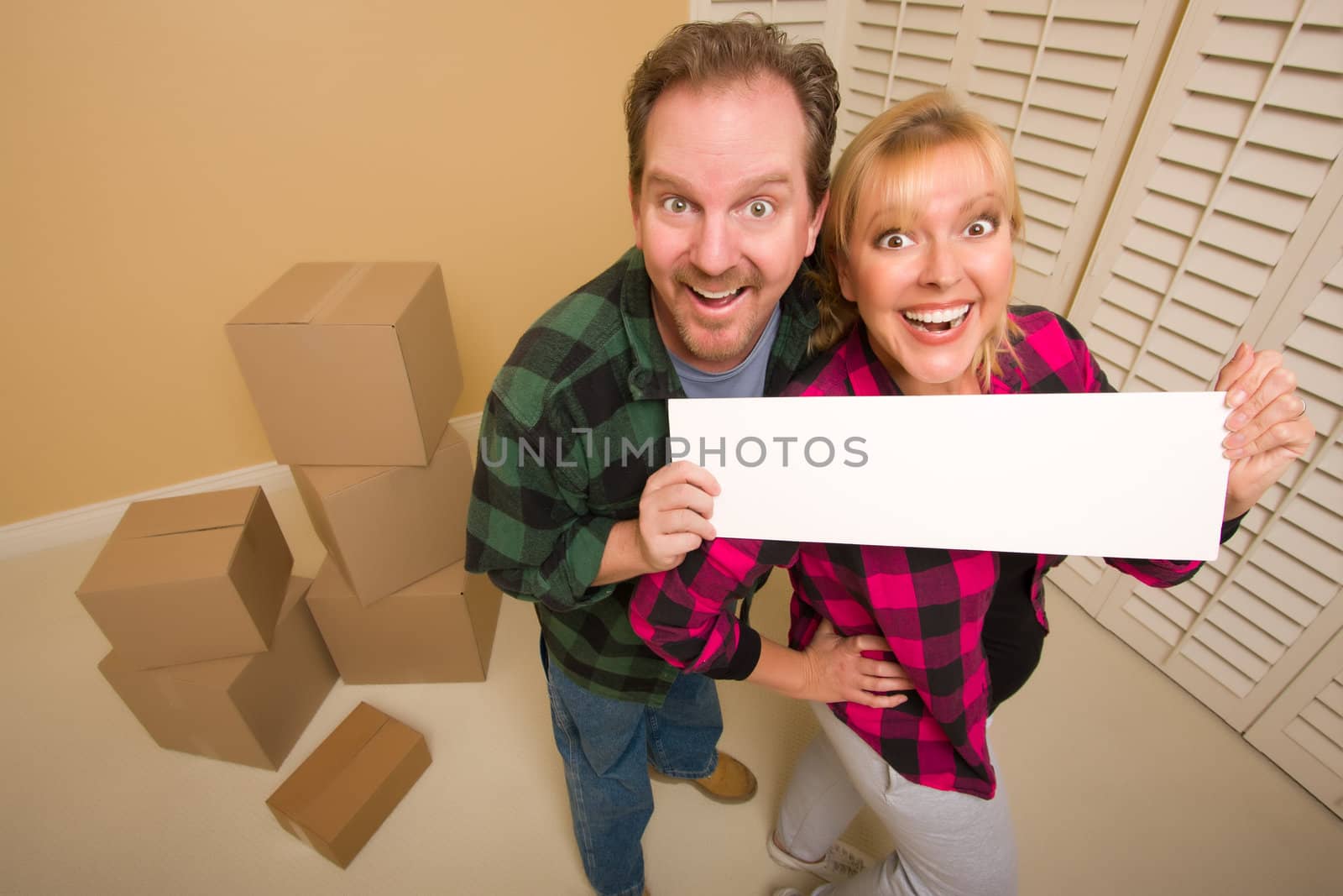 Happy Couple Holding Blank Sign in Room with Packed Boxes by Feverpitched