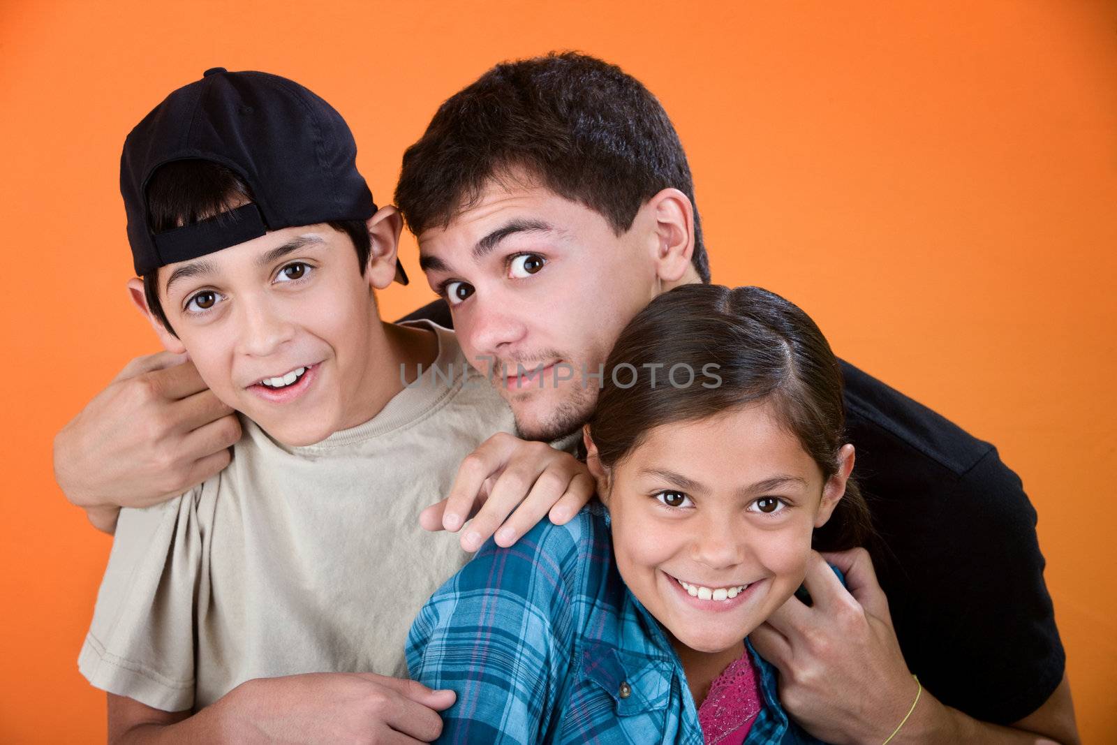Teen holding and playing with brother and sister on an orange background