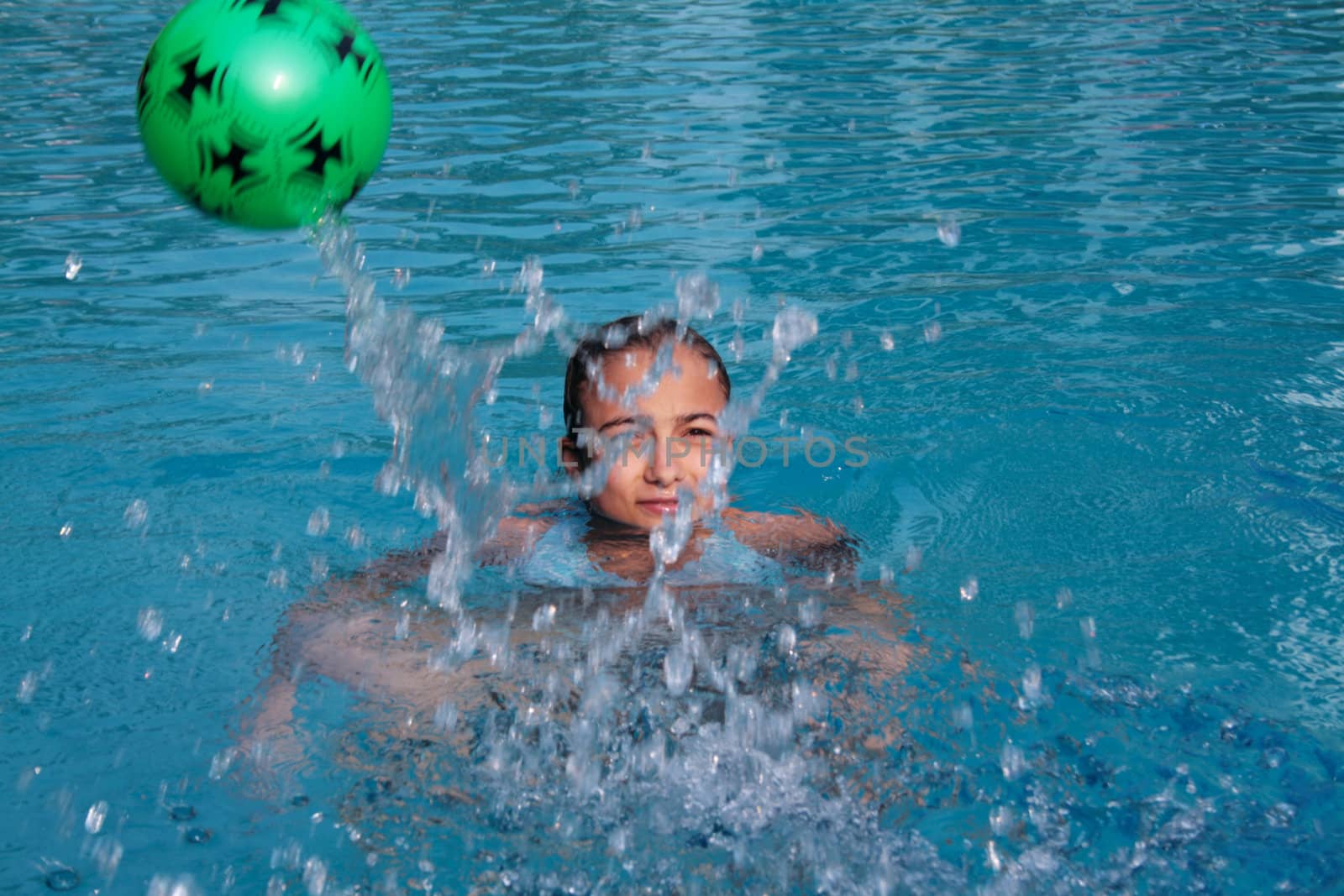 Beautiful, young girl in drop of water in pool with green ball