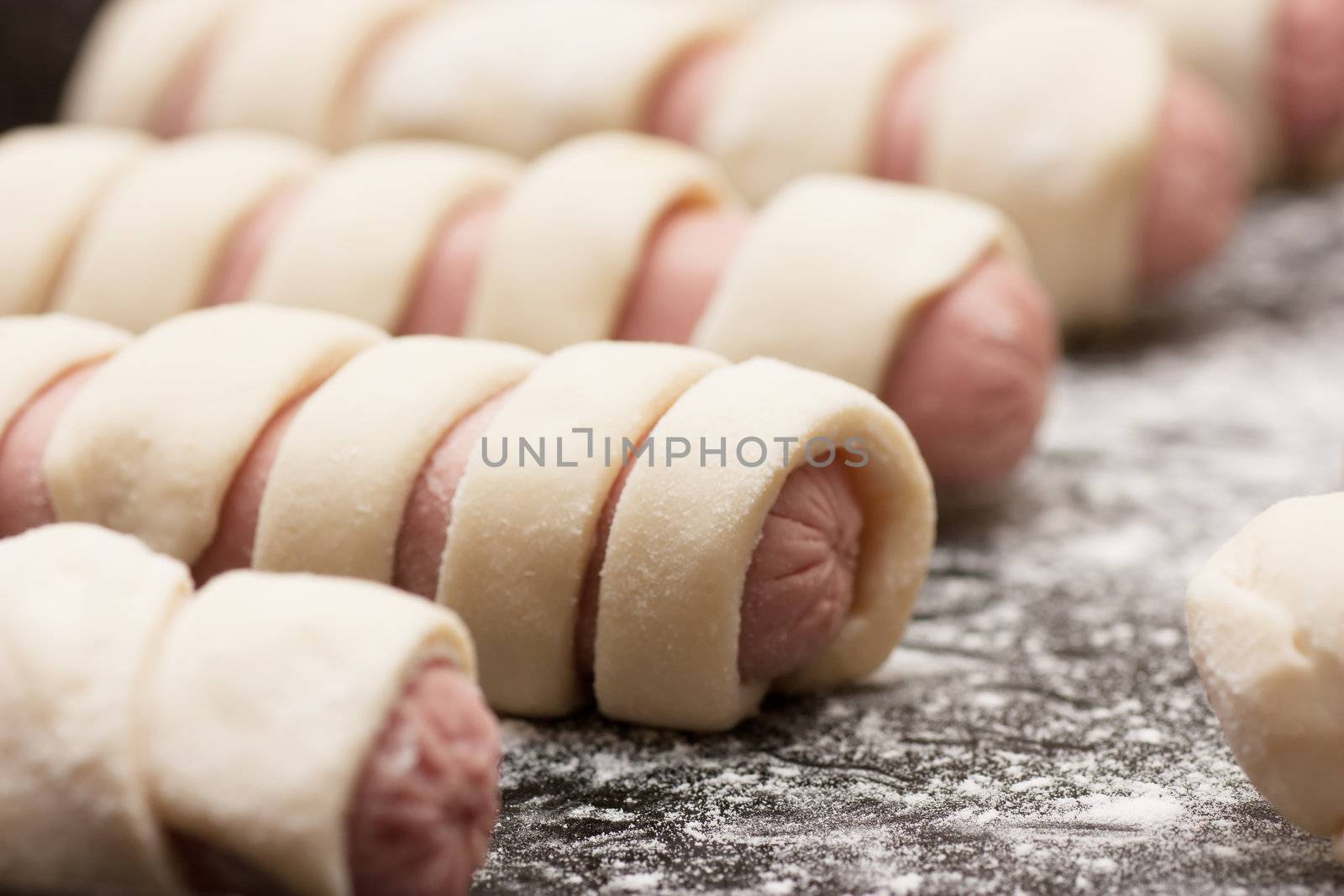 Raw sausage rolls in pastry on a baking tray
