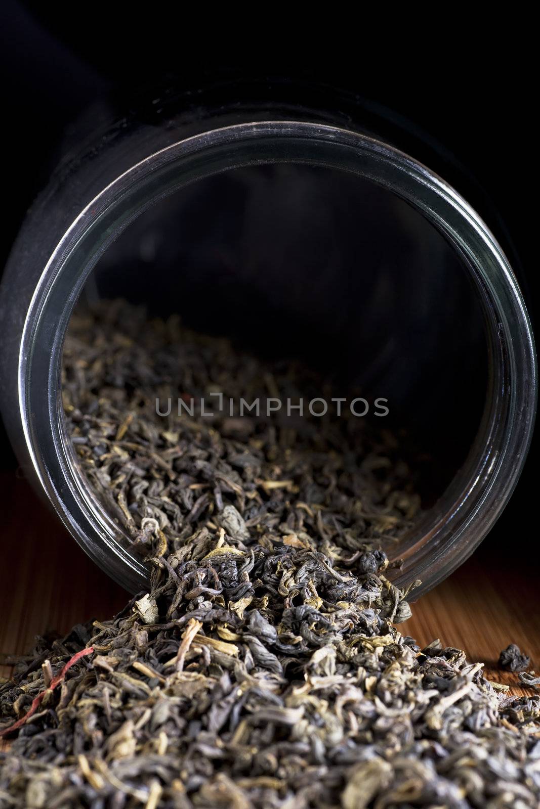 Dried Jasmine tea leaves spilling from jar with dark background.