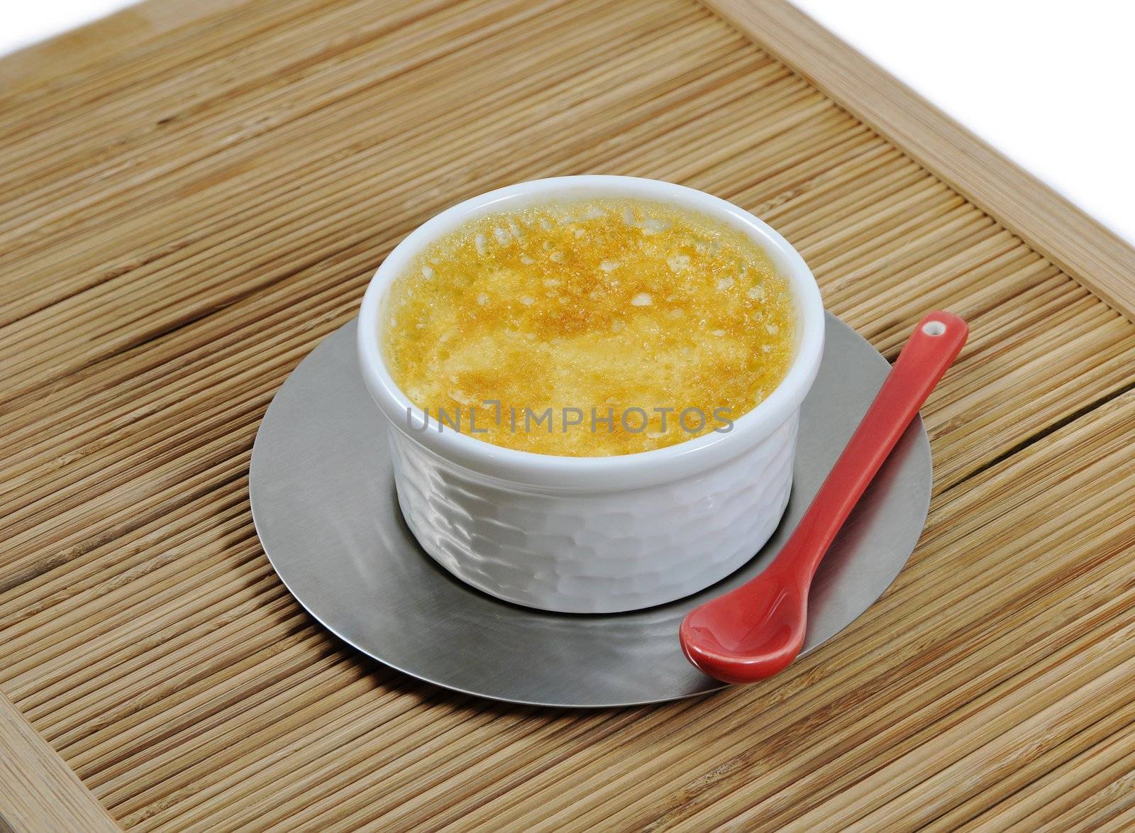 Custard with an iron steel saucer and a red ceramic spoon on a bamboo tray