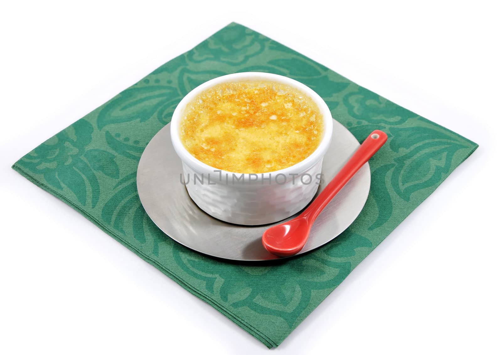 Custard with a little red ceramic spoon on a green paper napkin and a white background