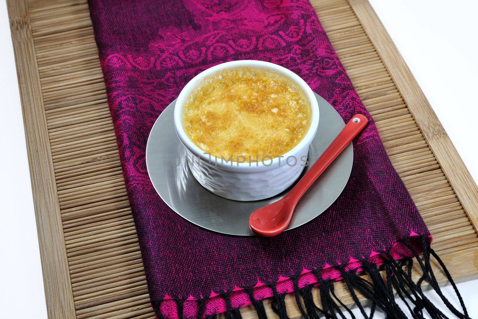 Indonesian tablecloth with a home-made custard and a little red ceramic spoon on a bamboo tray