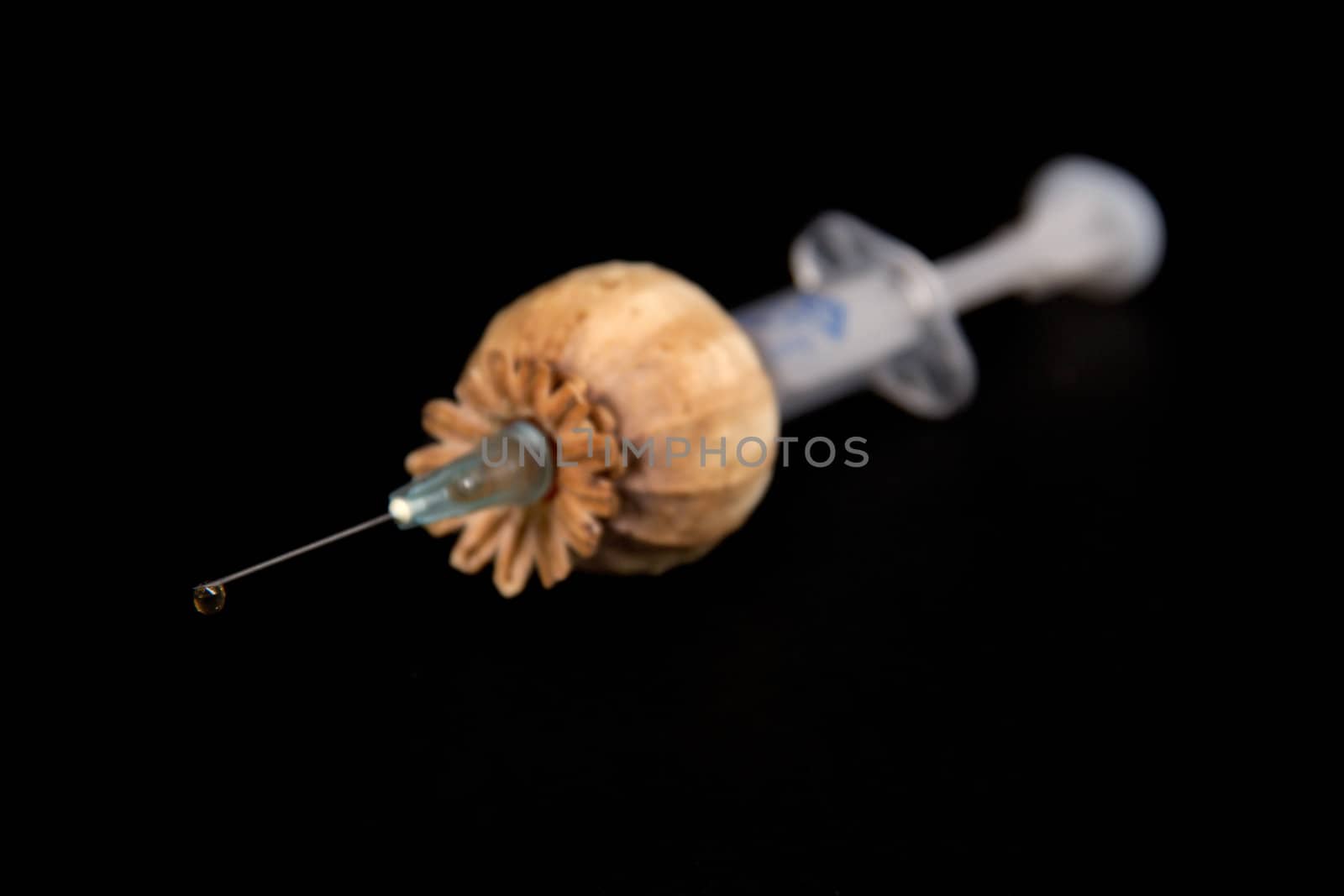 Syringe with an injection of the drug made of a poppy, on a black background.