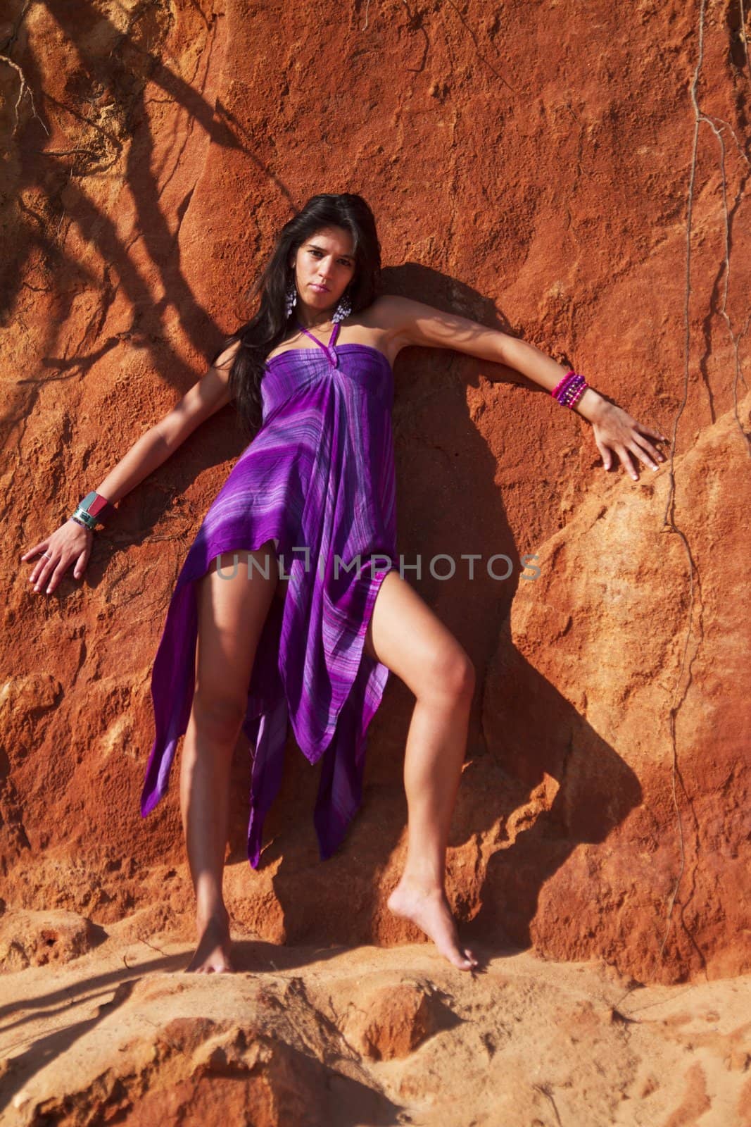 View of a beautiful young girl posing with a purple dress next to a cliff on the beach. 