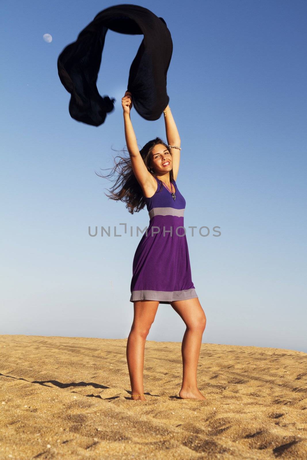 View of a beautiful young girl playful with a purple dress in the beach.