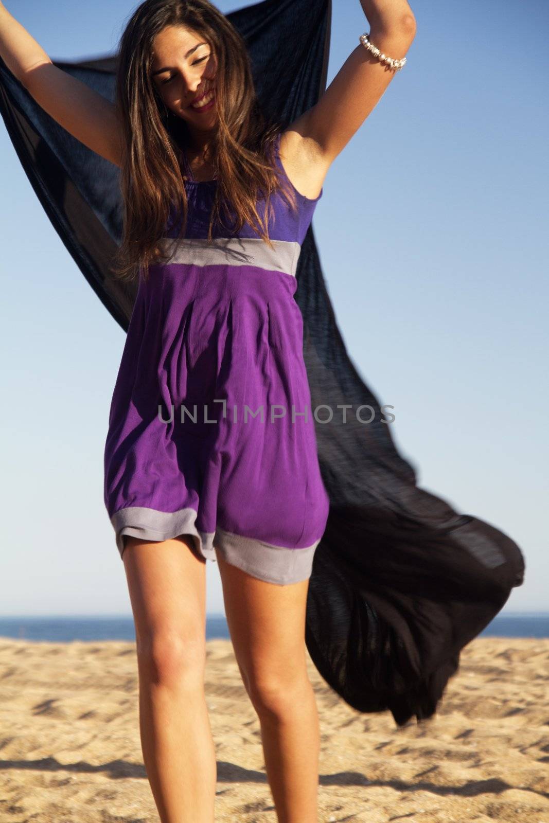 View of a beautiful young girl playful with a purple dress in the beach.