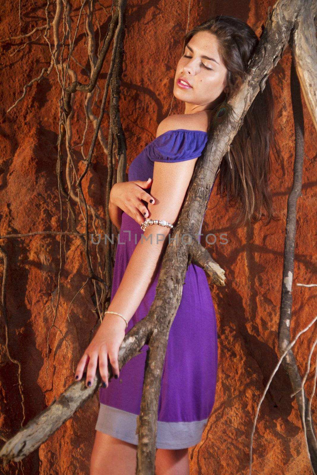 View of a beautiful young girl with a purple dress standing on a red cliff on the beach.