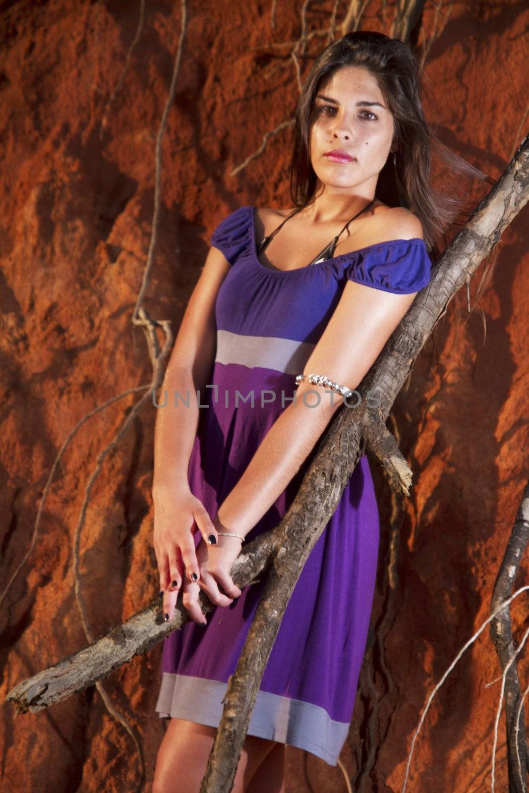 View of a beautiful young girl with a purple dress standing on a red cliff on the beach.