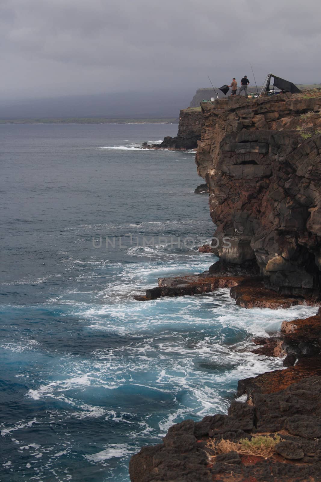 fisherman on top of cliff fishing in the Pacific Ocean in Hawaii as storm approaches by njene