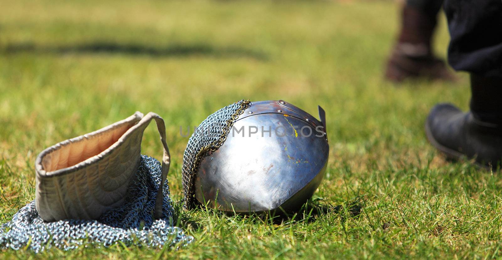 Image of a steel helmet and a chainmail hood on a filed after a medieval fight in a sunny day.