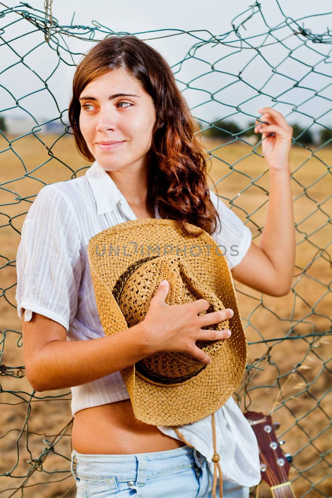 View of a beautiful young country girl with a guitar on the fence of the grassland. 