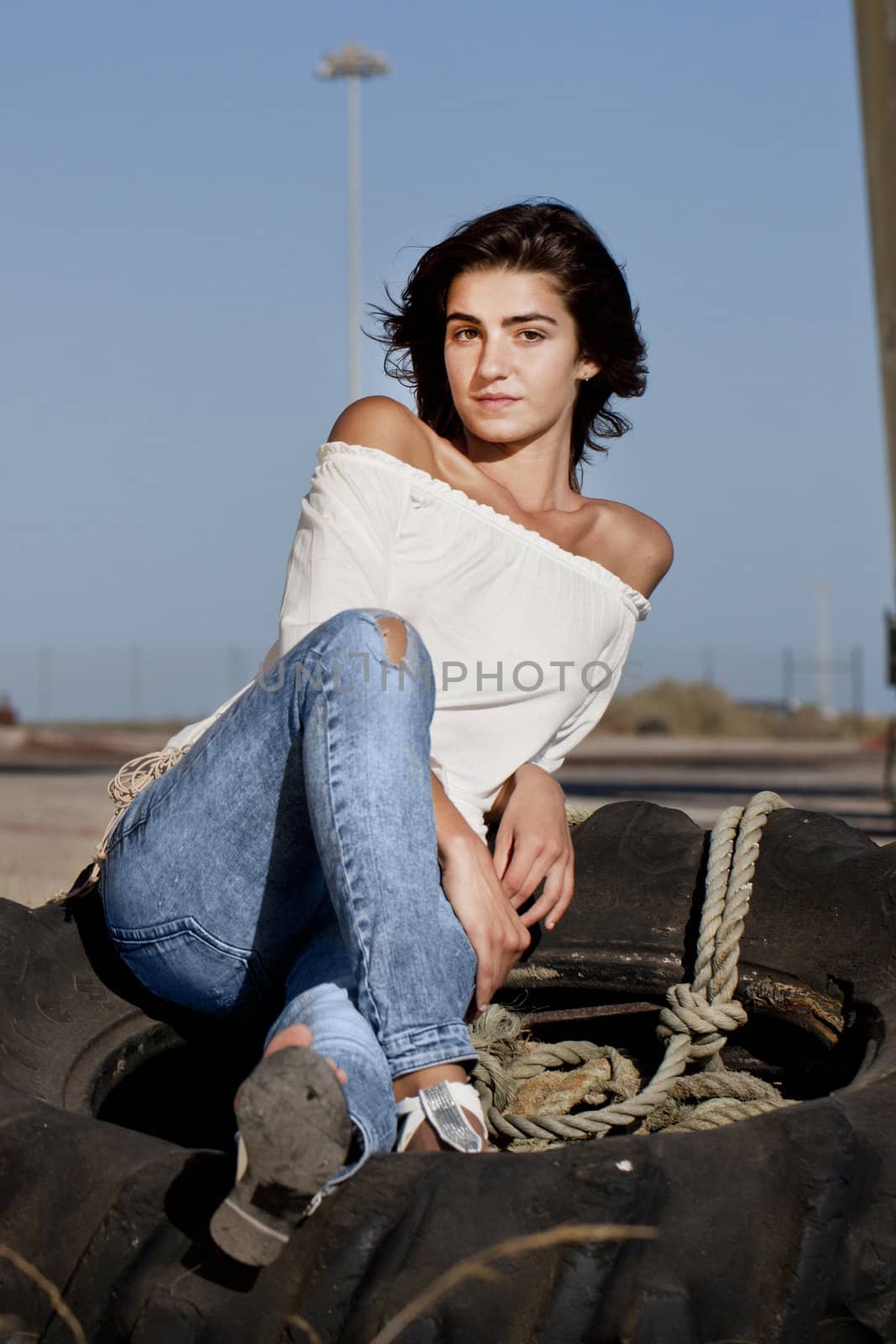 view of a beautiful young teenager sitting on top of an abandoned tractor wheel.