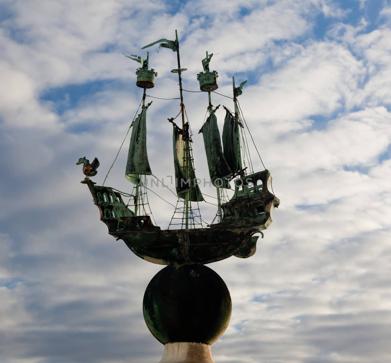 Small copper sailing ship set against a cloudy blue sky and showing its green colored copper sheen