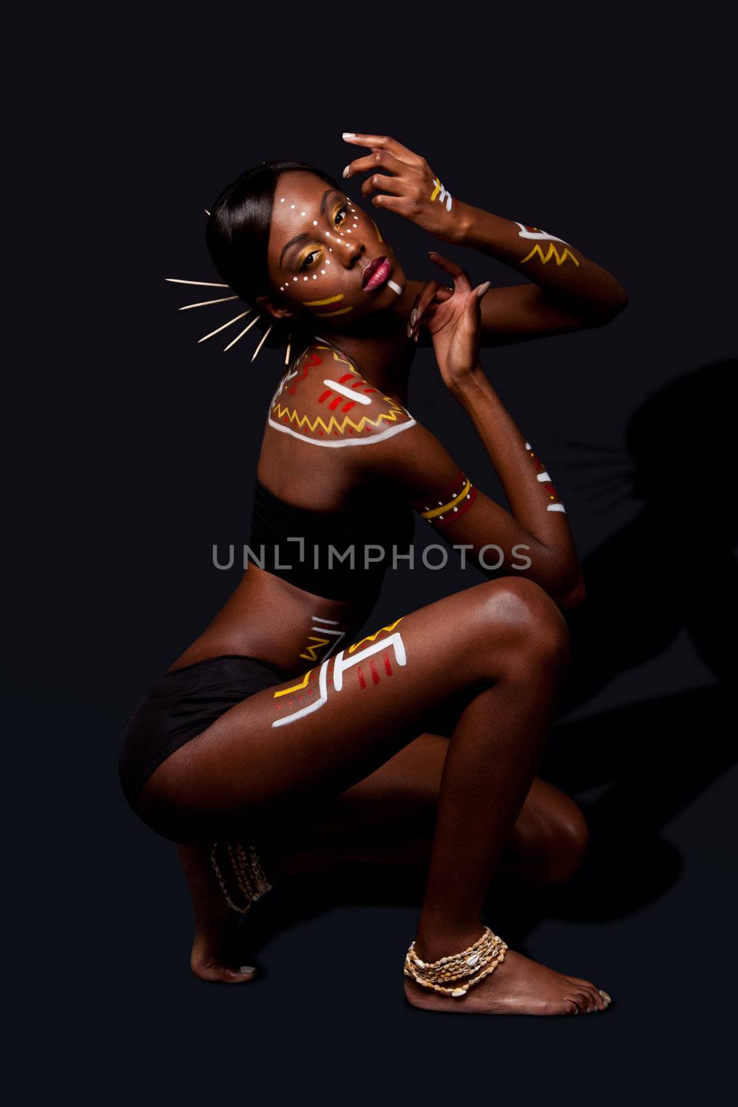 Beautiful exotic African female fashion with tribal yellow red and white makeup cosmetics and sticks in hair, in cultural dance position.