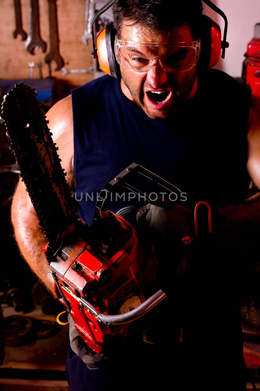 View of a angry garage mechanic man holding a chainsaw.