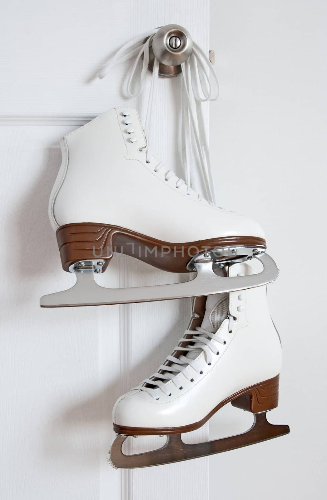 Elegant white figure skates hanging on a door knob.