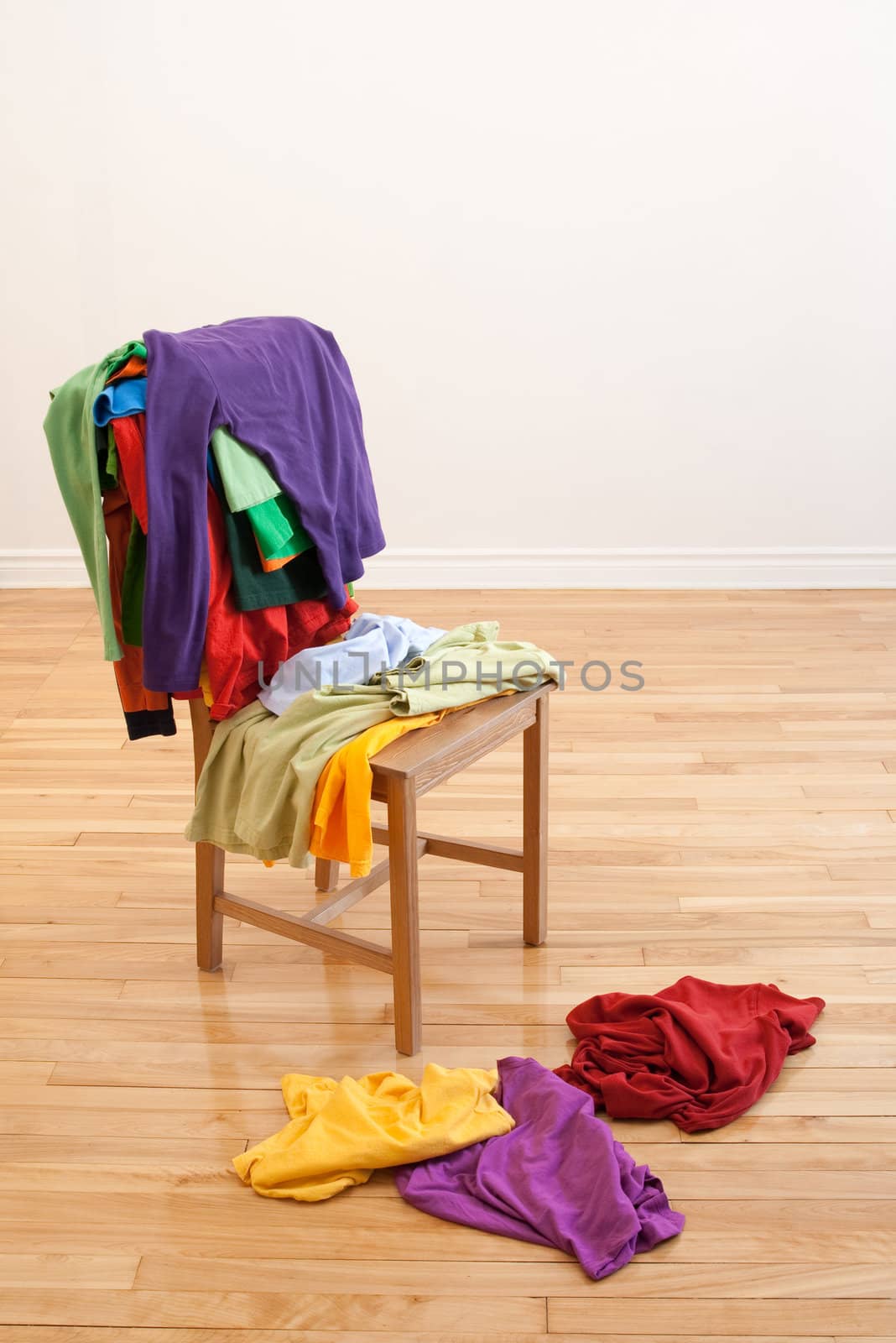 Lots of colorful messy clothes on a chair and on a wooden floor.
