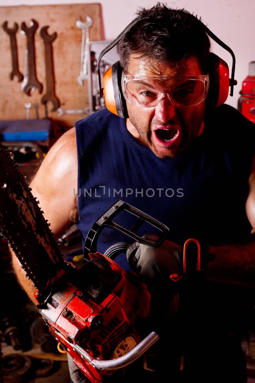 View of a angry garage mechanic man holding a chainsaw.