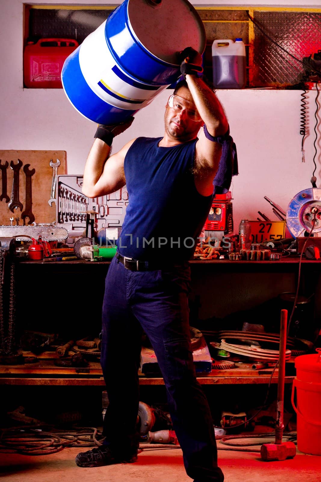 View of a happy garage mechanic man holding an oil barrel.