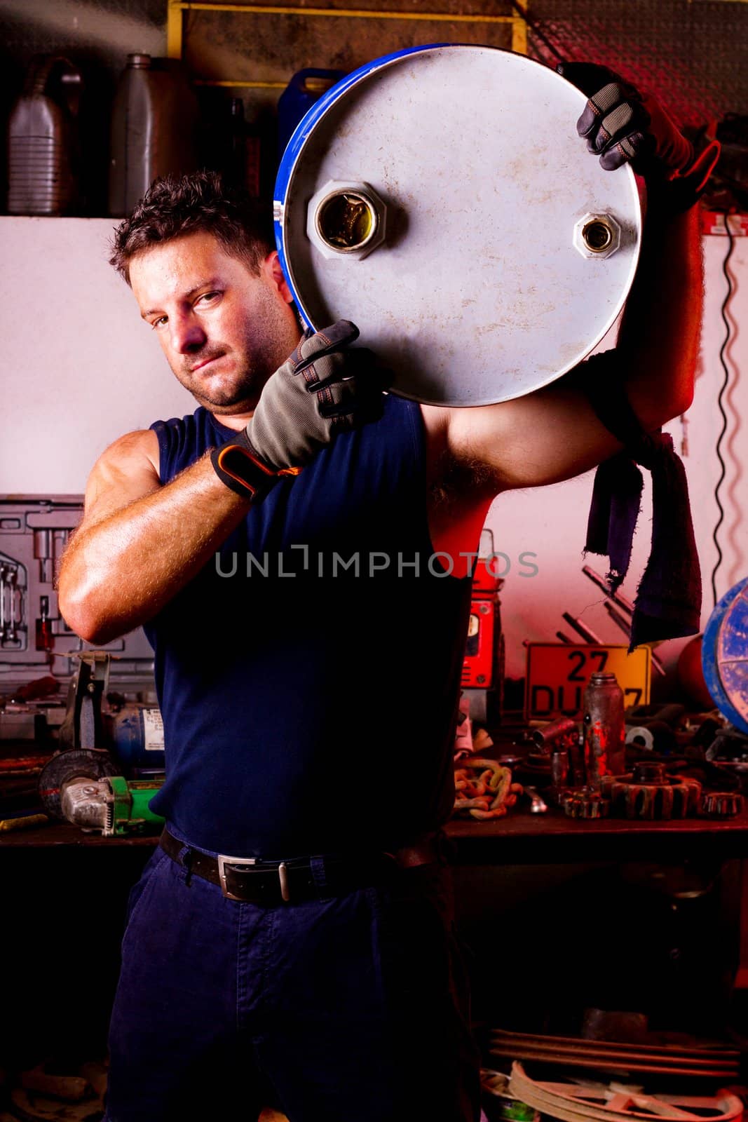 View of a happy garage mechanic man holding an oil barrel.