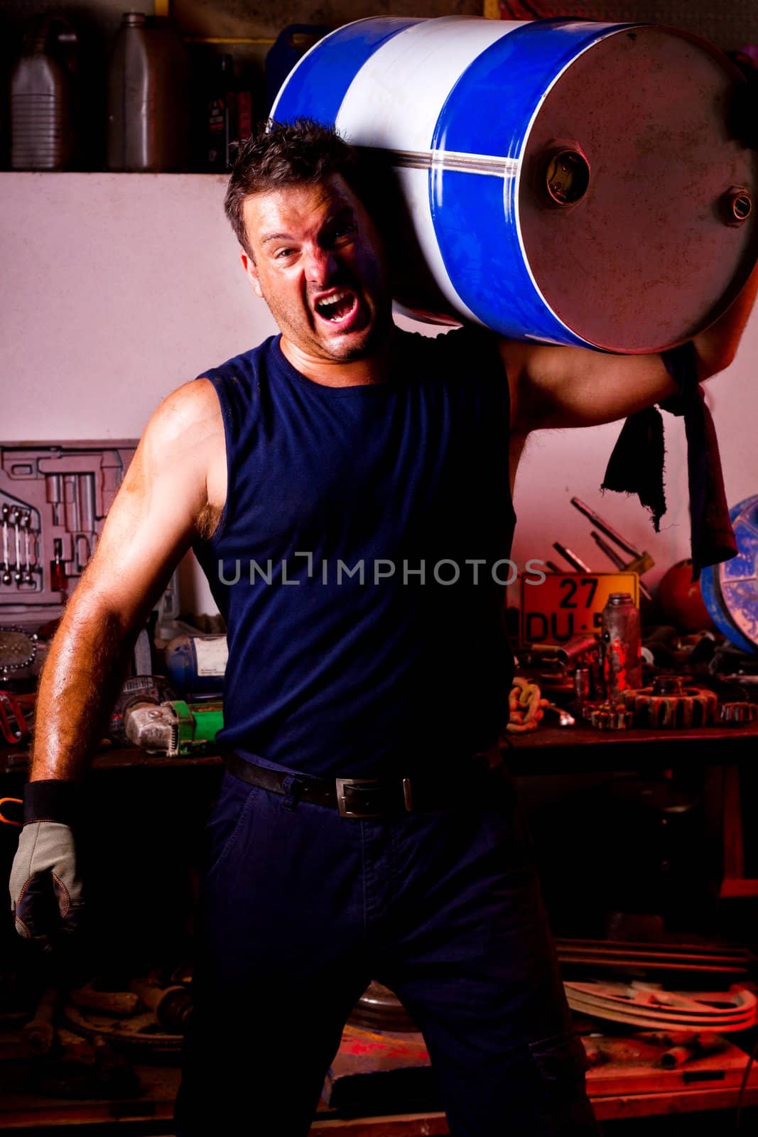 View of a happy garage mechanic man holding an oil barrel.