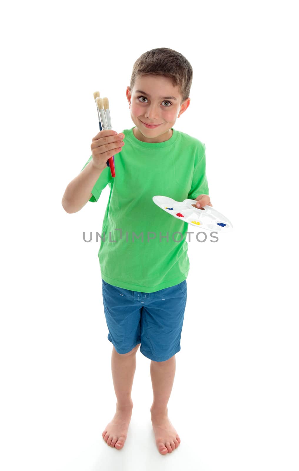 A young boy stands holding or showing paints and paint brushes.  White background.