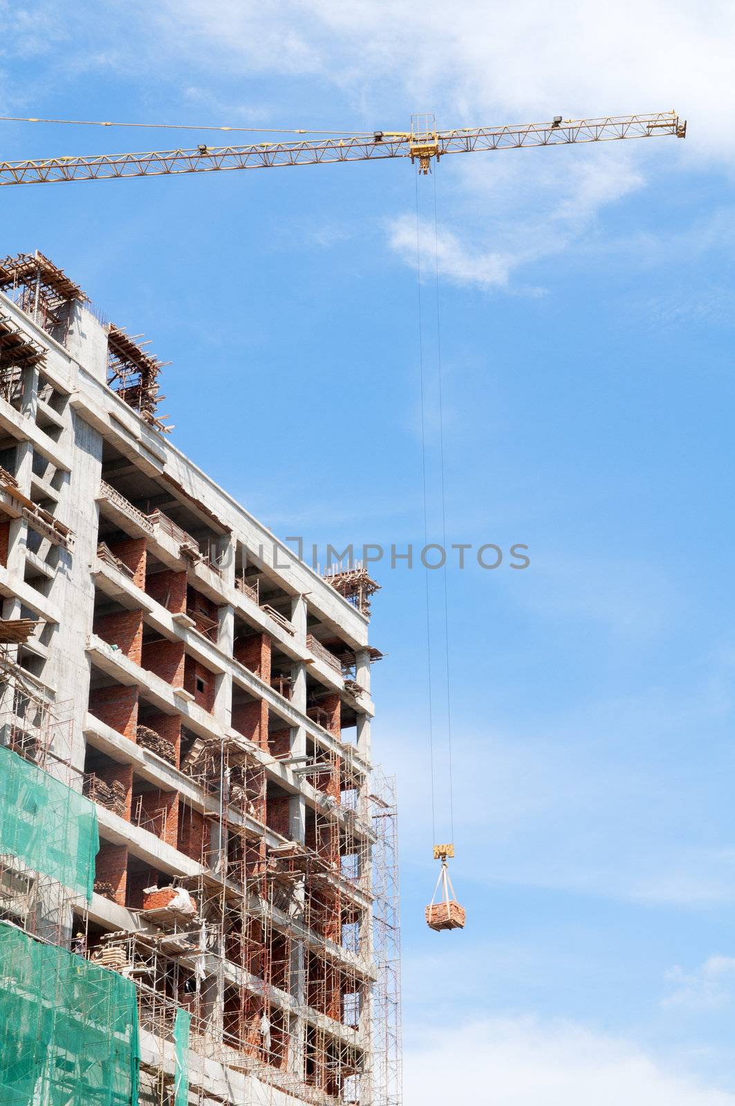 Highrise building under construction with crane against blue sky.