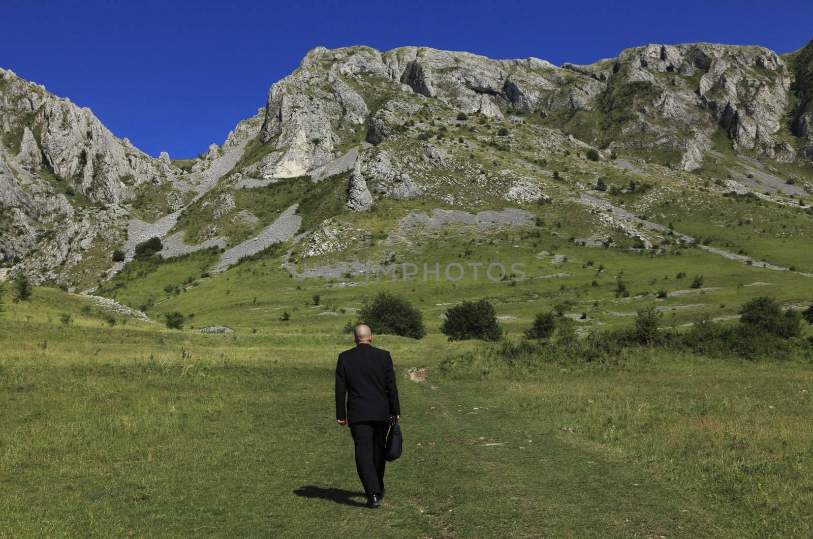 Businessman oudoors walking through a big mountain.The main focus is on the rocks,the man is slighty out of focus.