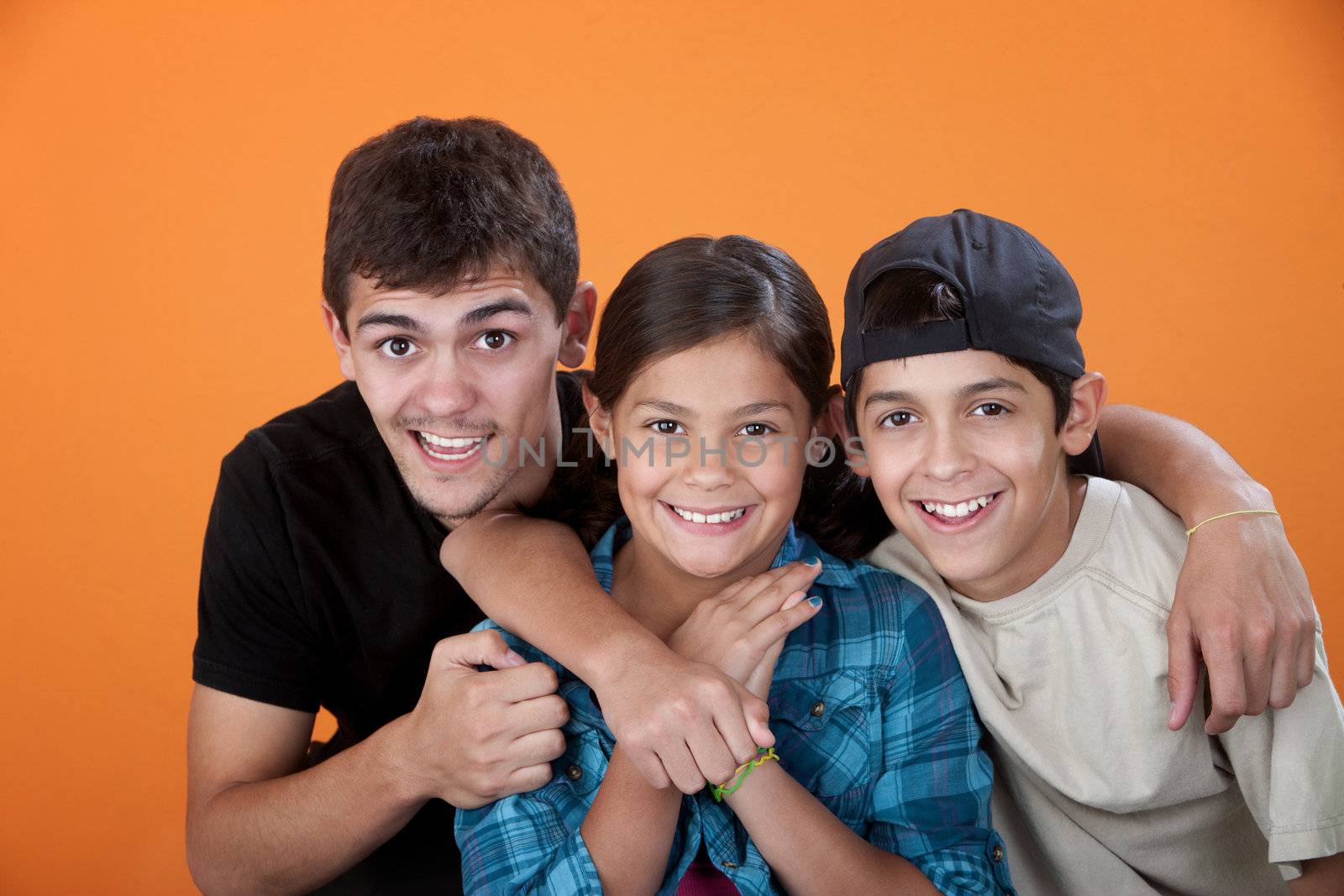 Big brother with two siblings smiling on orange background