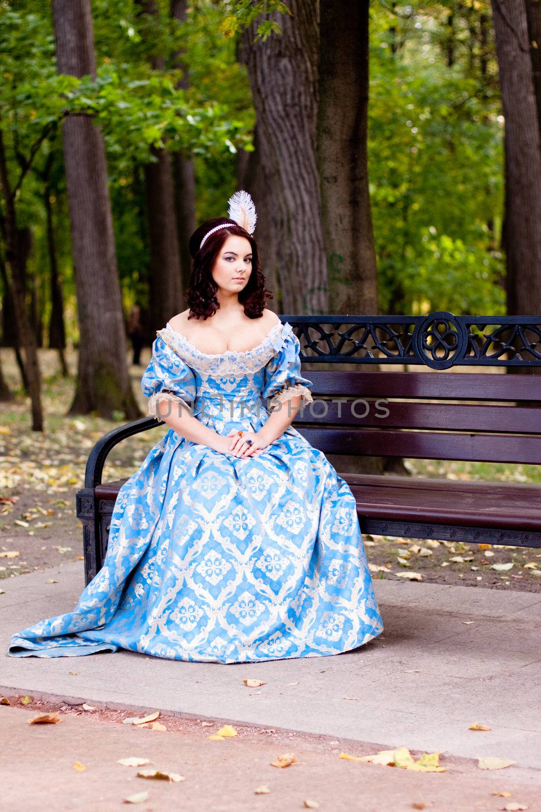 A portrait of lady in a blue baroque dress sitting on bench
