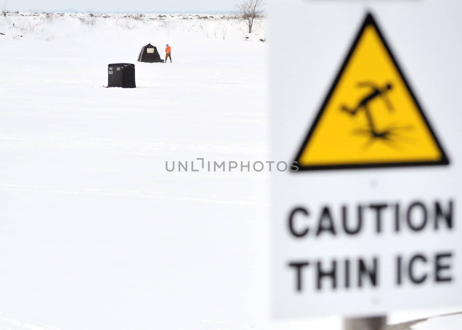 A thin ice warning sign for frozen lake with ice fisherman on the lake.
