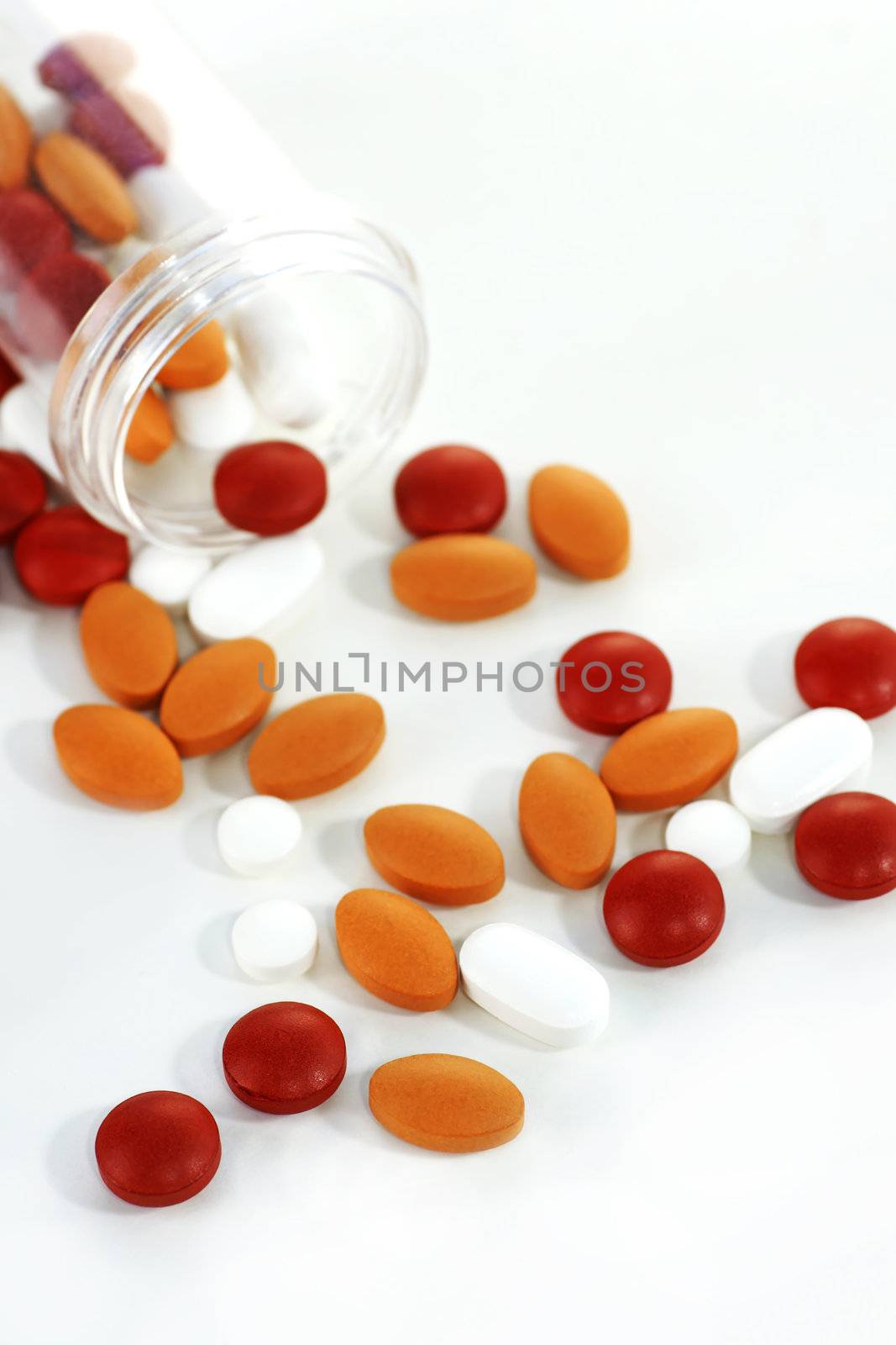 Health concept: high key picture of colorful pills with open plastic bottle barely visible on stark white sterile background with slight shadows.