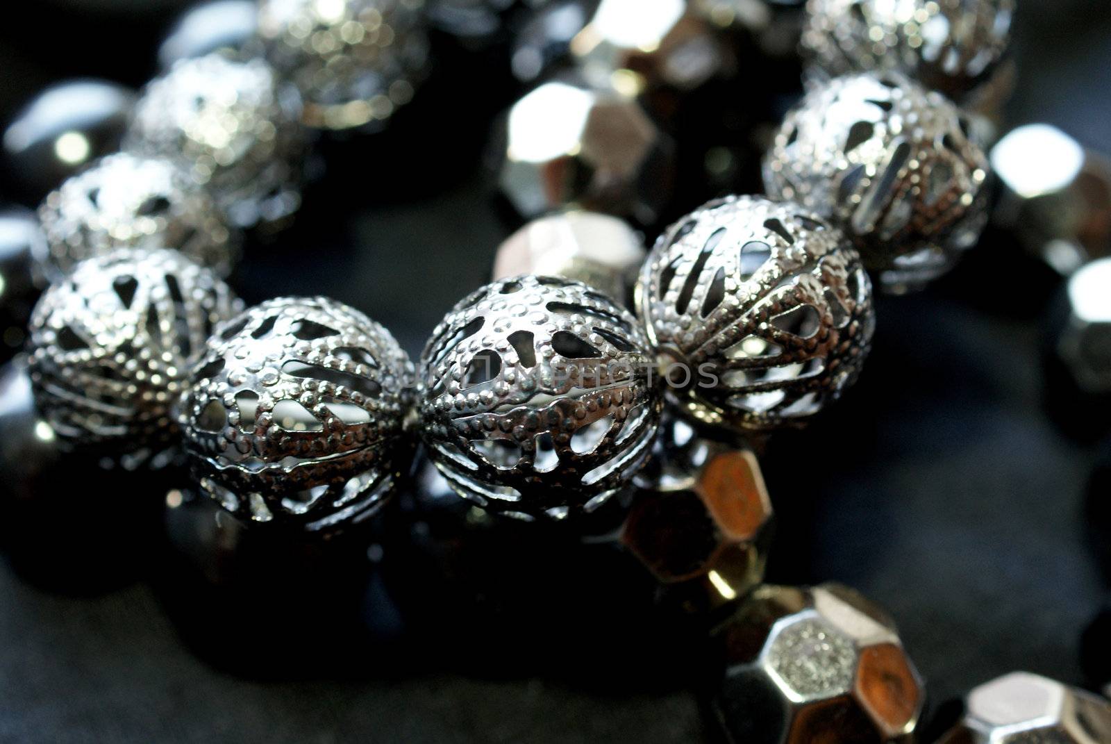 A close up of a bracelet with shiny dark silver beads over black. Soft focus, bokeh effect. 