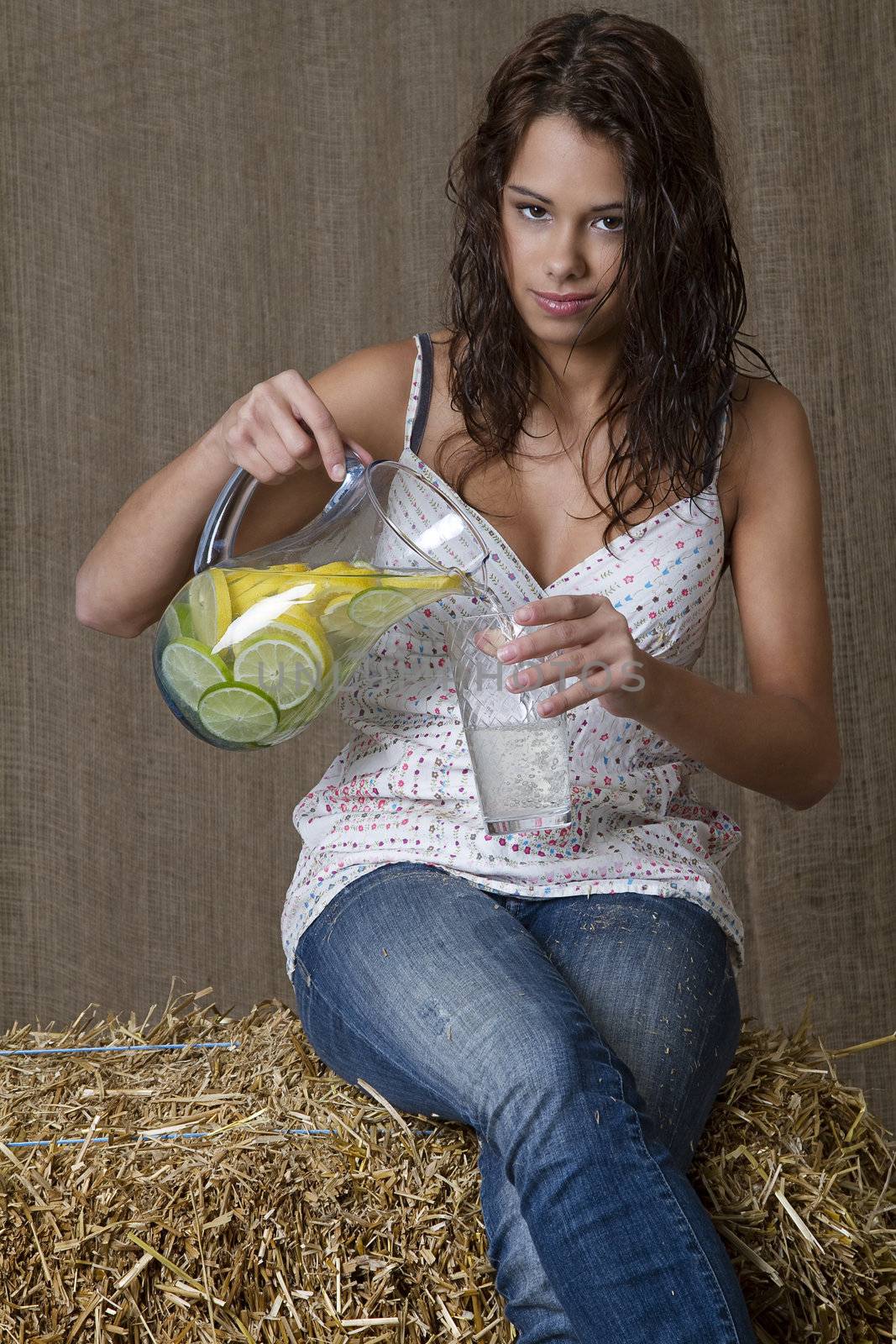 brunette woman sitting on bales of straw pouring a glass of lemonade