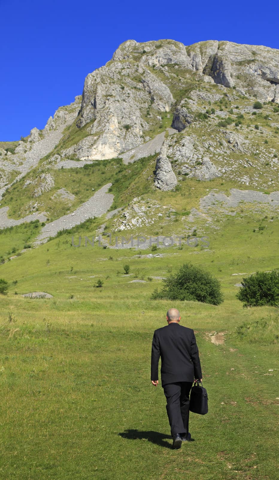 Businessman oudoors walking through a big mountain.The main focus is on the rocks,the man is slighty out of focus.