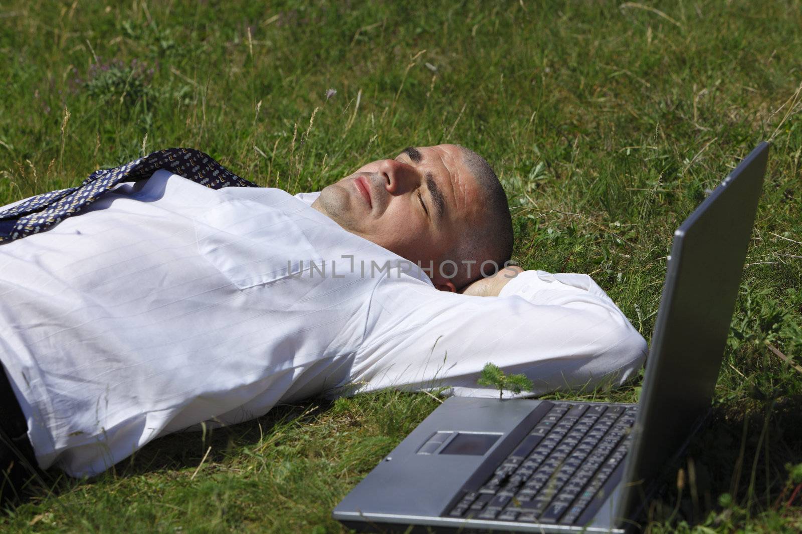 Tired man sleeping in a field near his laptop.