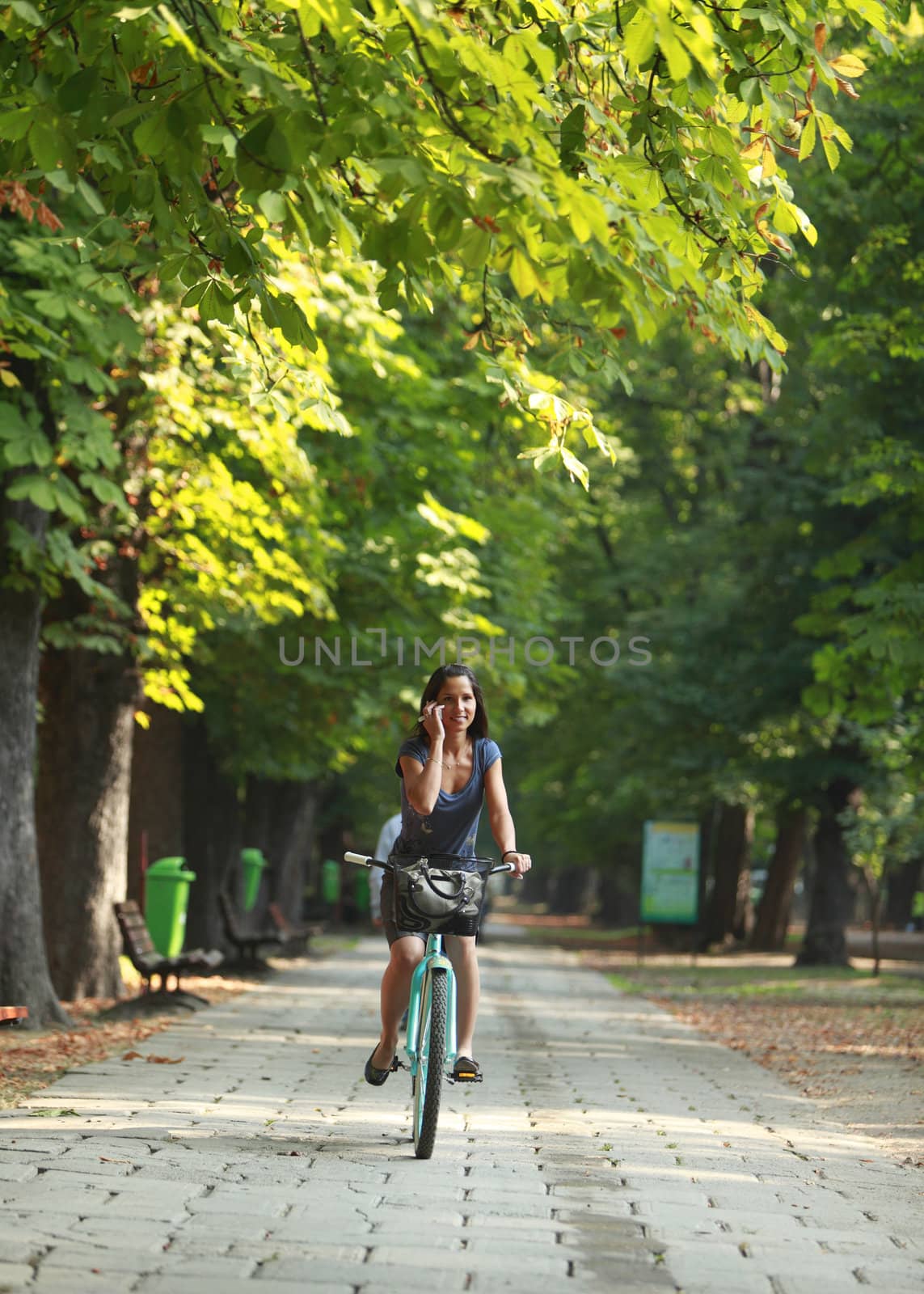 Image of a woman on the phone riding a bicyclein an autumn park
