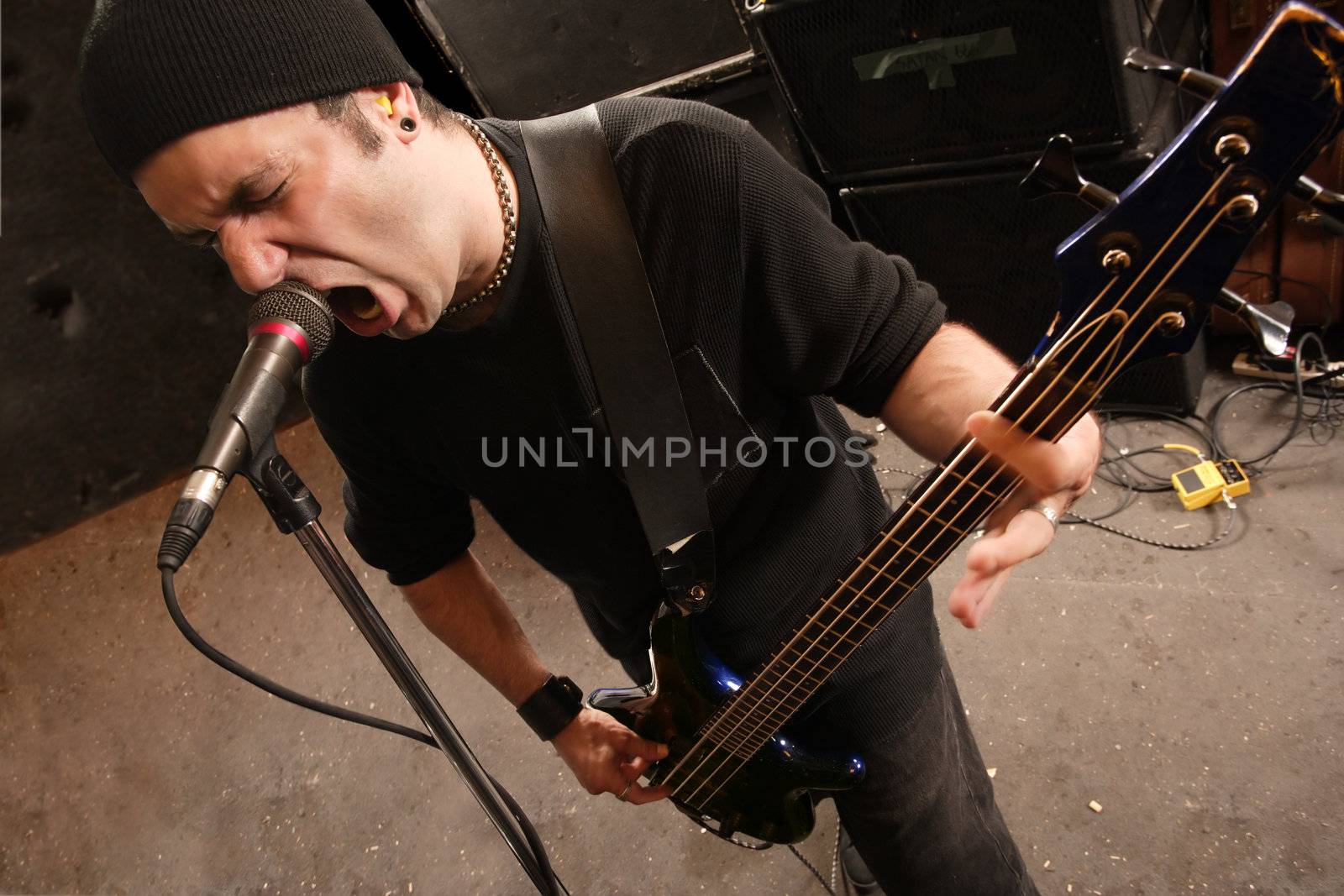 Bassist playing and screaming into a microphone. 
