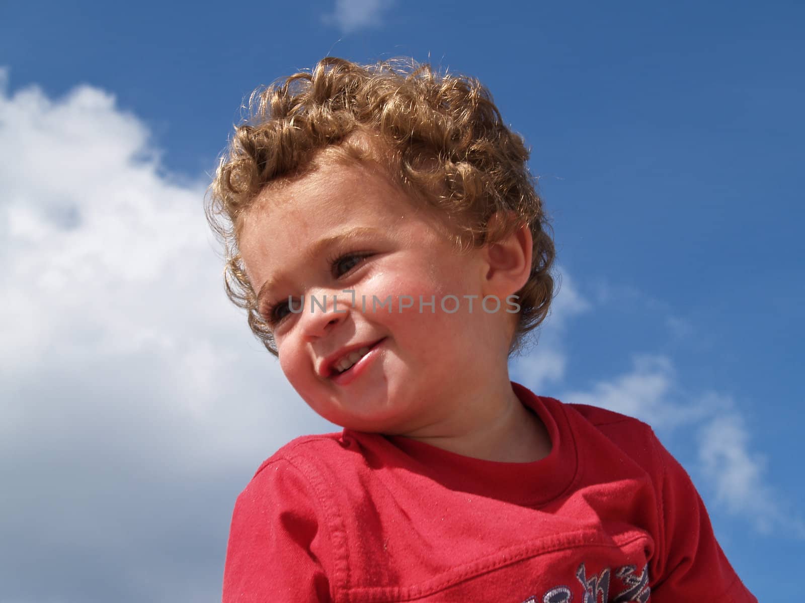 Young boy looking right under sky with white clouds.