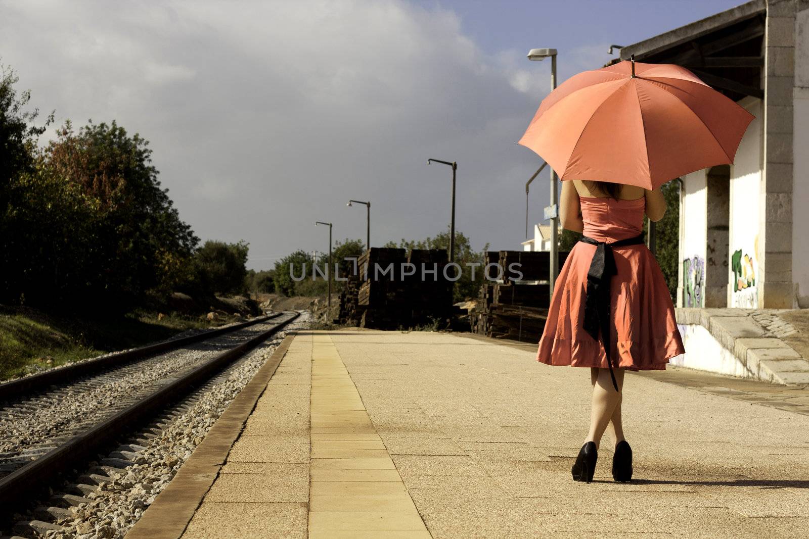 View of a beautiful woman with red dress and umbrella on a train station.