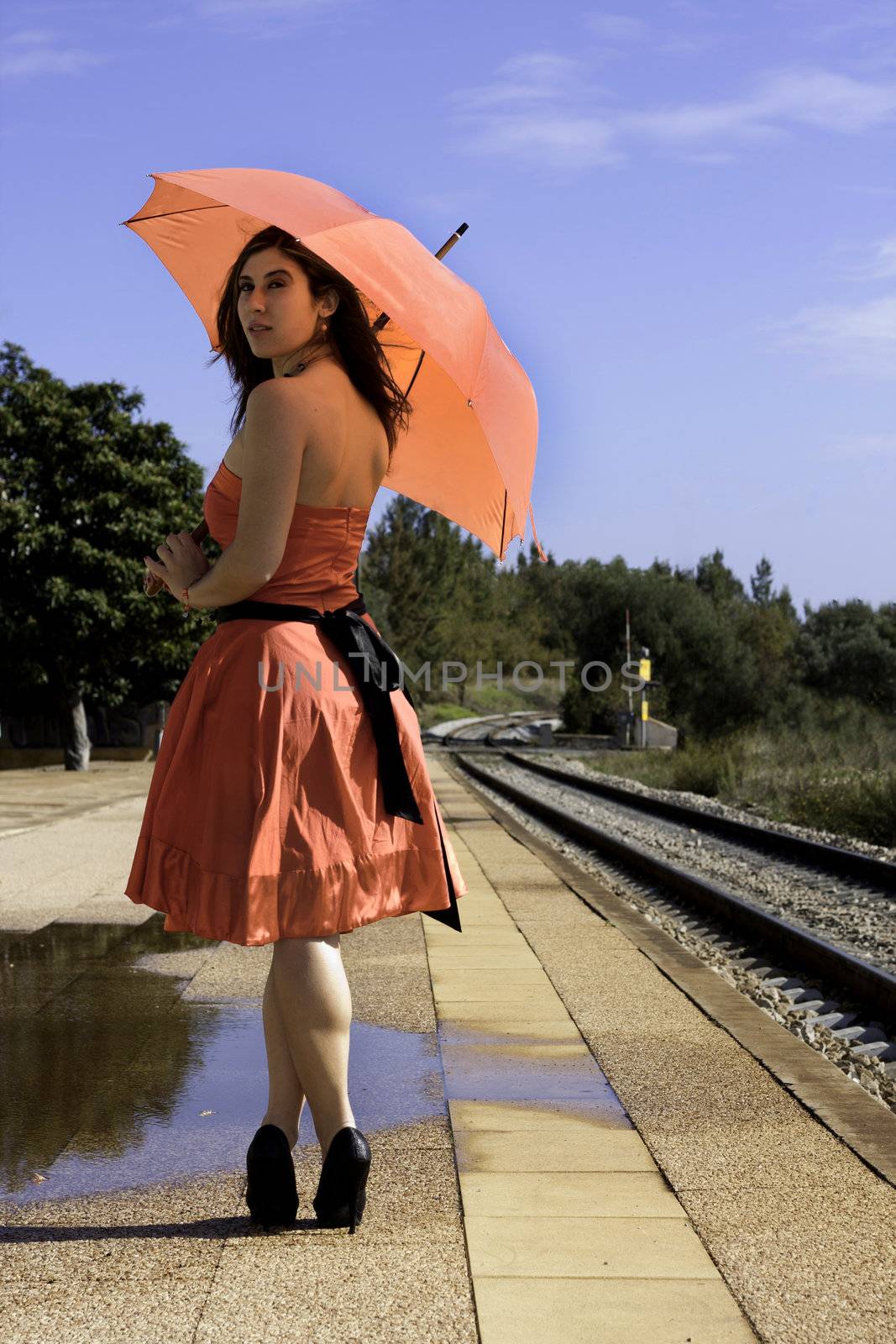 View of a beautiful woman with red dress and umbrella on a train station.