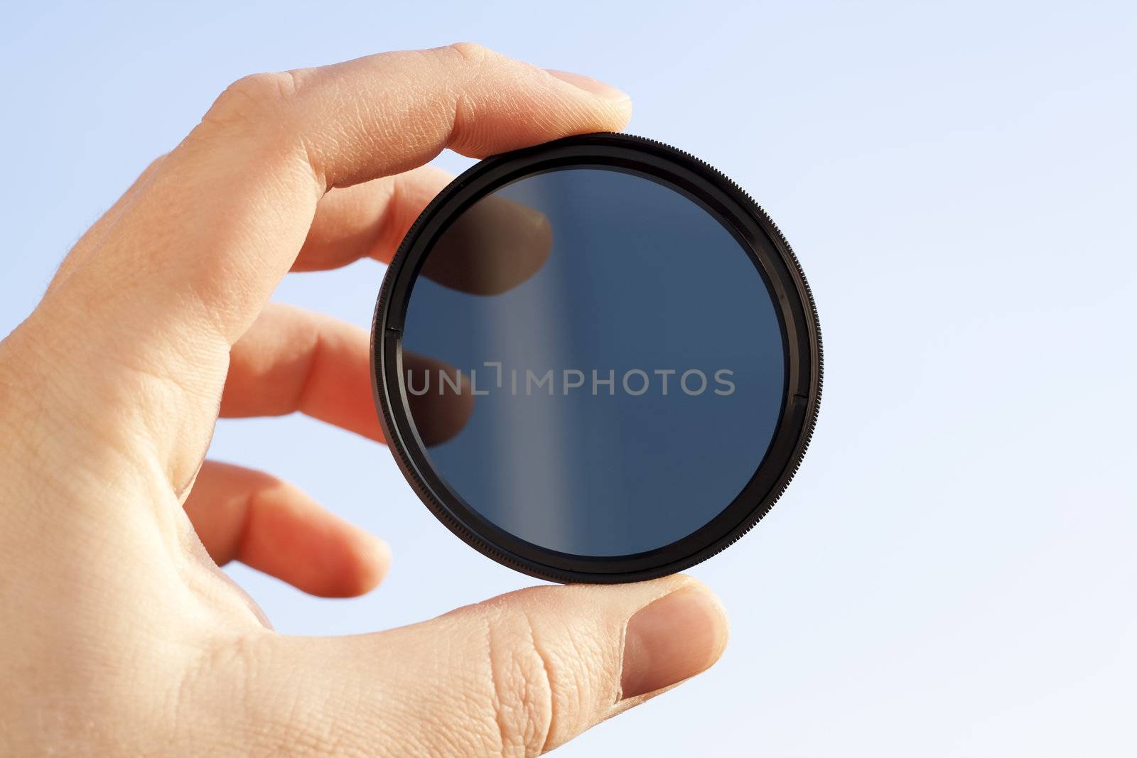 Man's hand holds a ND (neutral density) optical filter against sky