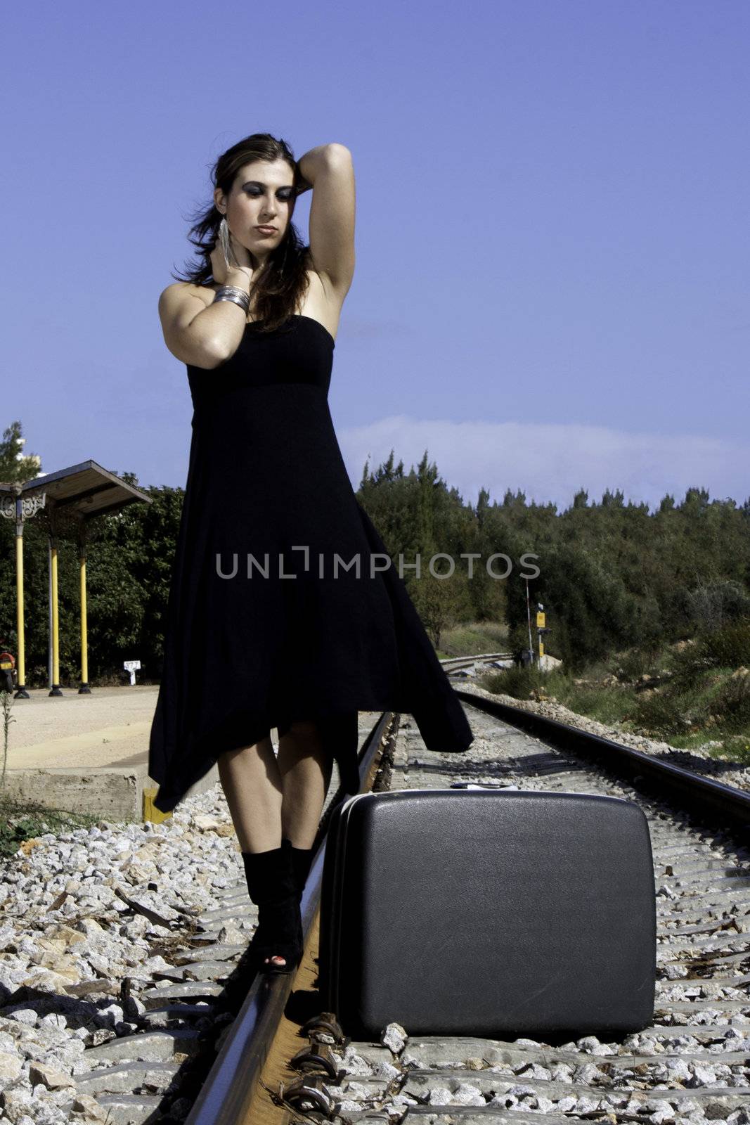 View of a beautiful woman with black dress with a travel case on a train track.