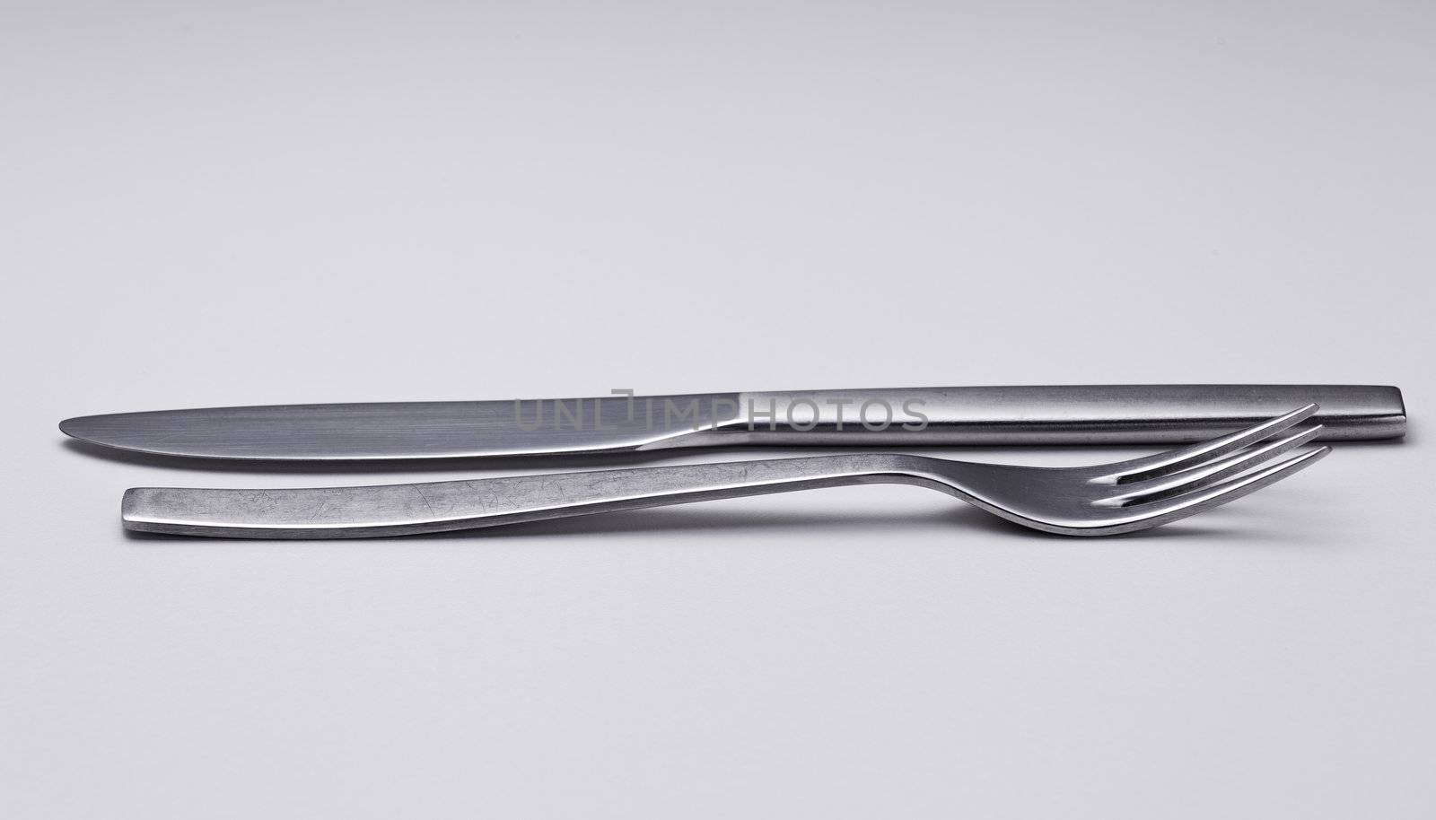 Knive and fork from modern stainless steel design isolated against white and reflecting white  light