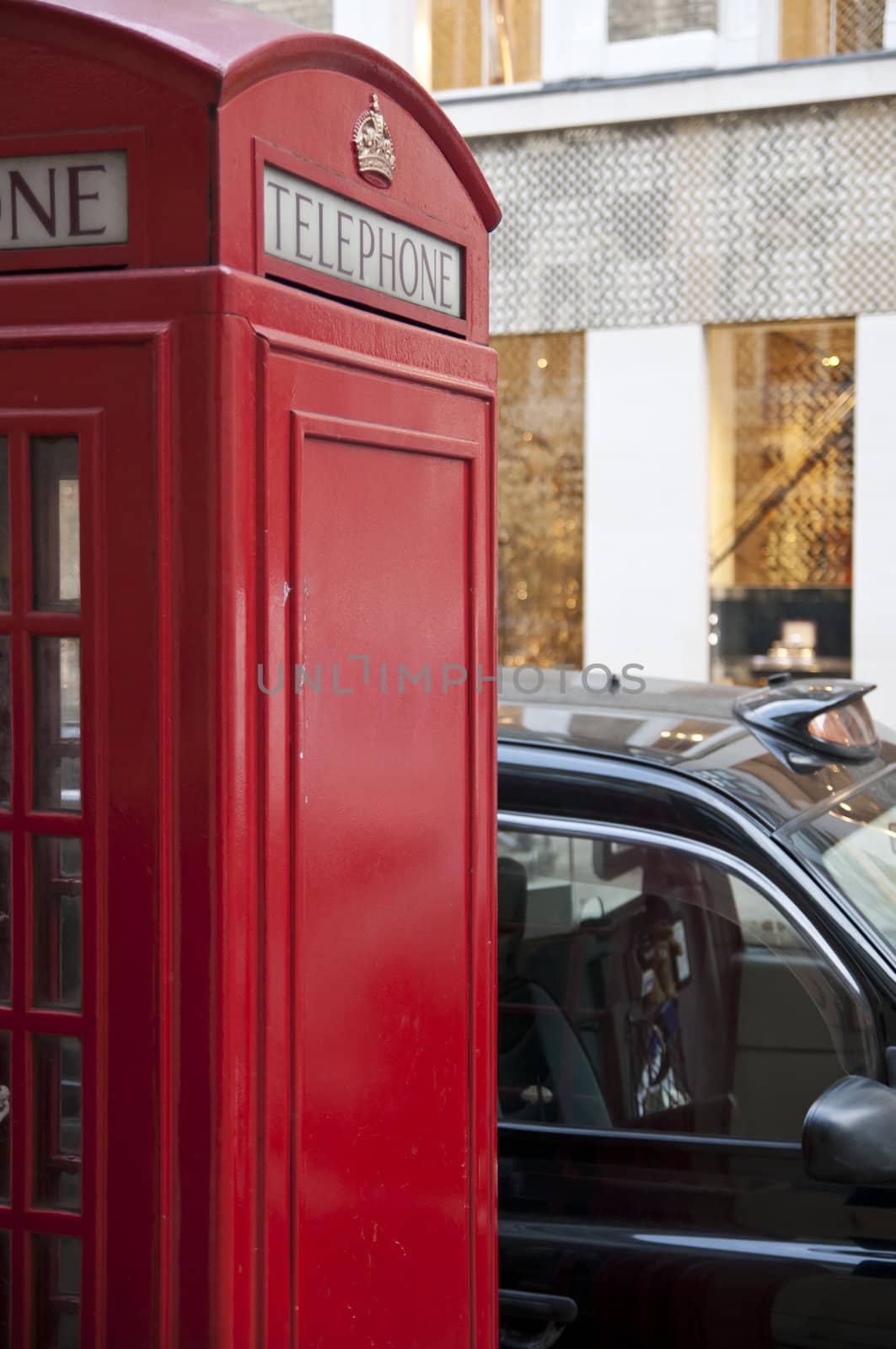 Cropped shot of a traditional red phonebooth with clear side as copy space in London, UK, with black cab parked nearby.