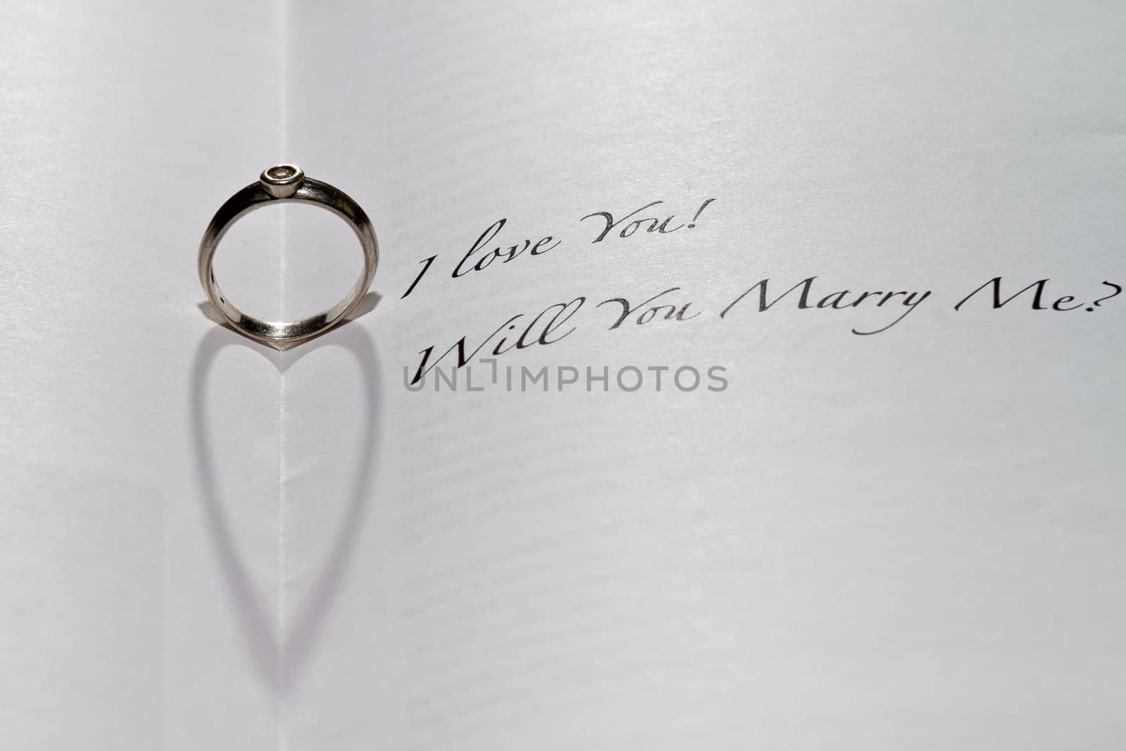 Ring casting heart shadow in book with the sentence "I Love You! Will You Marry Me?"