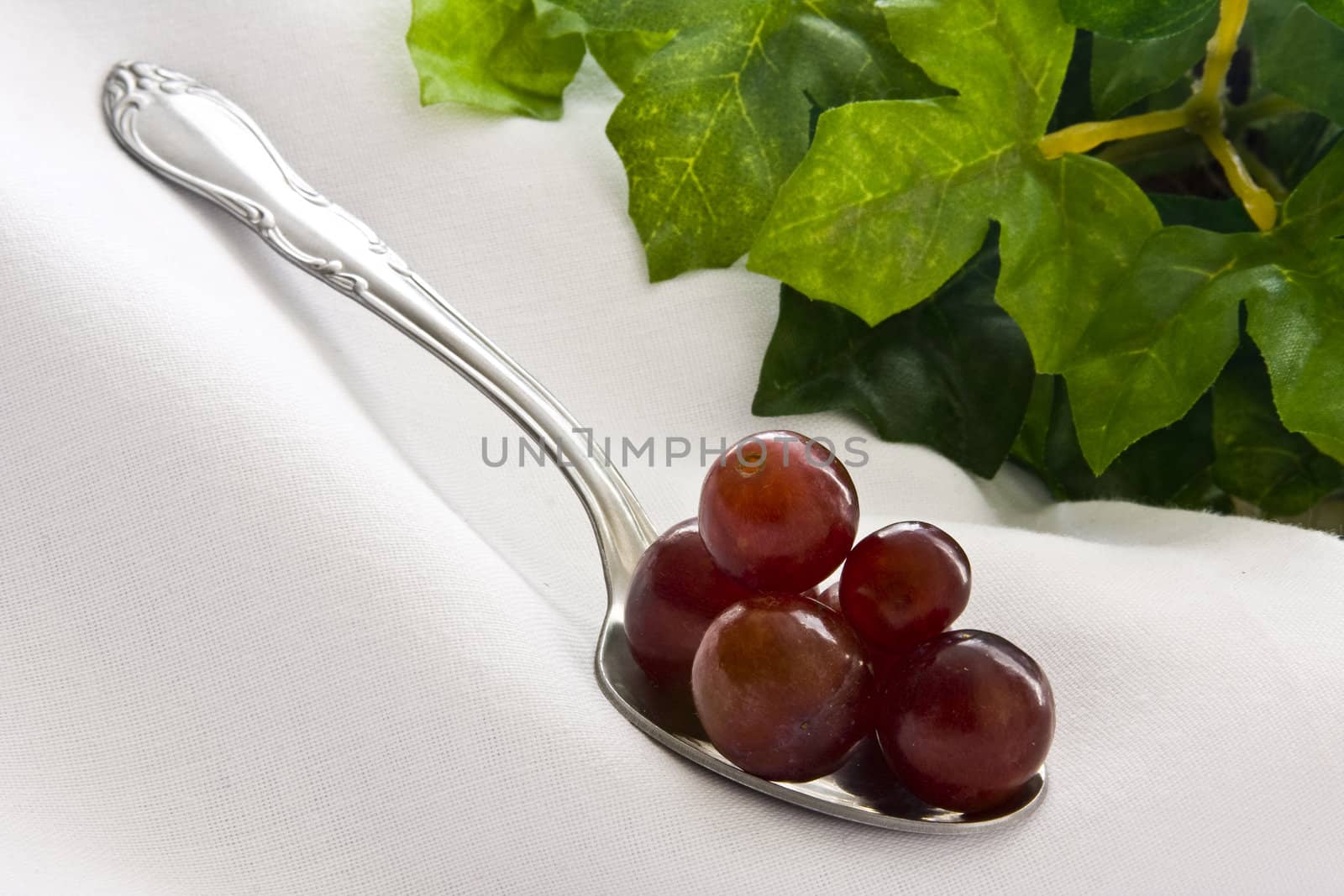 Red grapes piled on spoon on white cloth with leaves on background